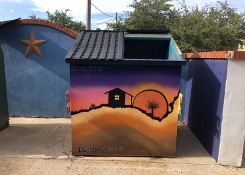 Garbage dumpster painted with Halloween scene of orange moon and haunted looking black house.