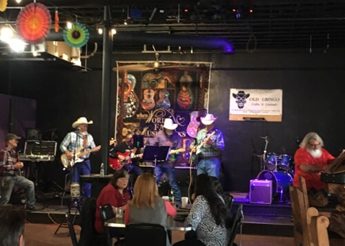 Country band playing on a brightly lit state, all four members have cowboy hats, beards and guitars.