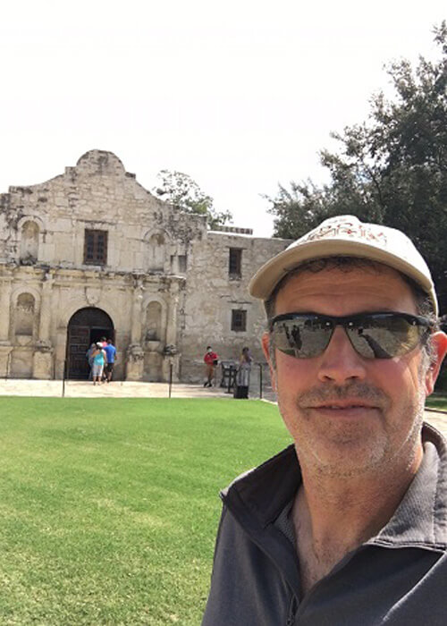 Picture of me smiling in front of The Alamo, a two story Mission style structure built in 1718. 