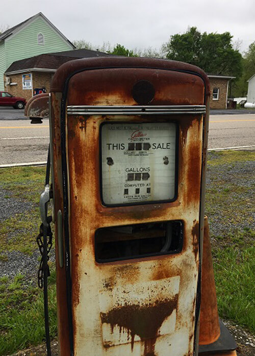 Close up of rusty 1960's-style gas pump, a couple buildings and grey sky in background.