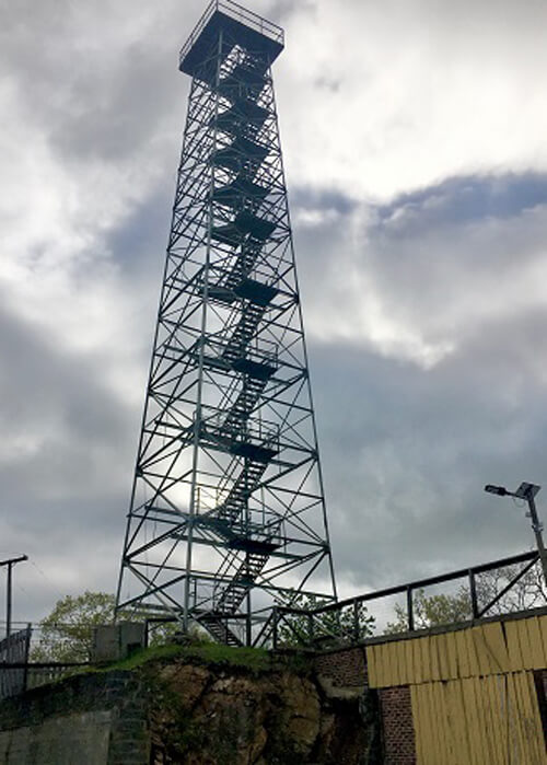 Twelve-story high lookout tower, stairs leading to the top. Sky covered in clouds in background.