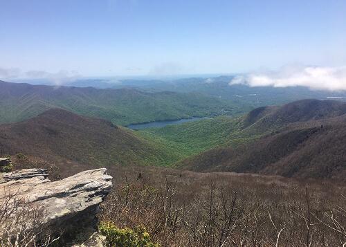 View from vista point on Mount Mitchell, overlooking green forest, a river, and clear blue sky.