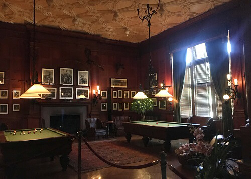 Indoor picture of the billiards room in the Biltmore Estate, with two billiards tables and red walls covered in photos and paintings.