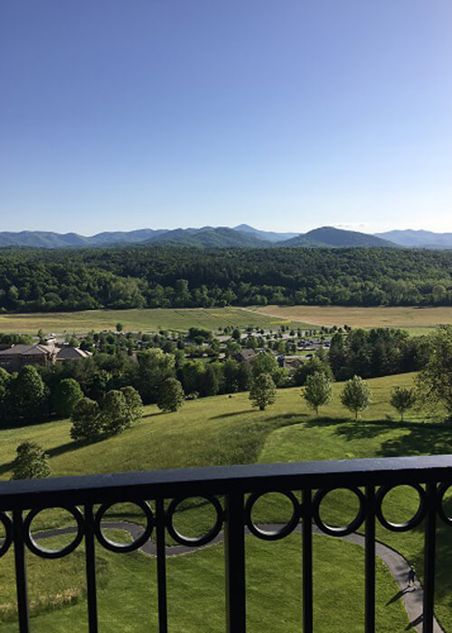 View over an iron balcony looking at rolling green hills with various species of trees on them.