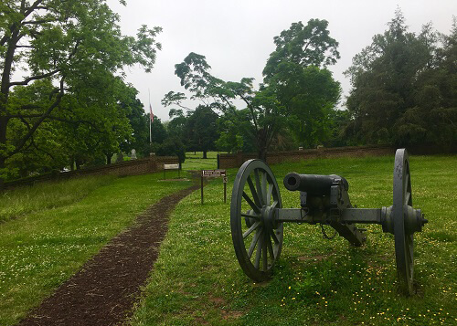 Civil war-era canon at bottom right on green grass, dirt walking path at left leading straight ahead.