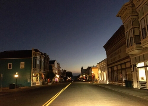 Looking down street at near-dark sunrise, Victorian style buildings on both sides of street.  