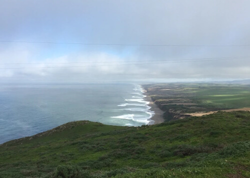 Overlooking miles of coastline from a green perch, cloudy sky above.