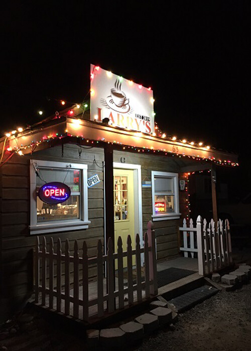 Night photo of small coffee shack with white bulb lights lining the roof and sign on roof saying "Larry's Coffee."