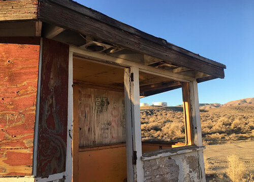 Abandoned drive-in ticket booth, which is a small wooden shack with peeling white and orange paint and no windows or doors. Blue sky in background.