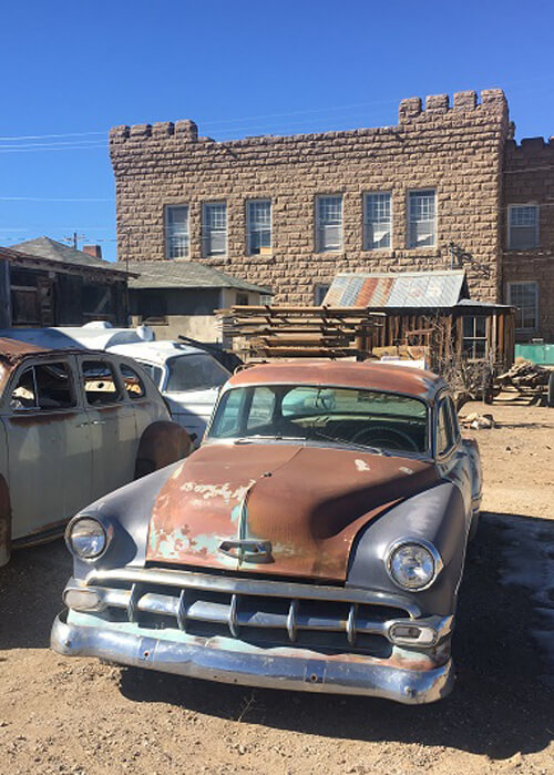 Front of 1950's Buick with two-story old adobe brick building in the background and blue sky above.