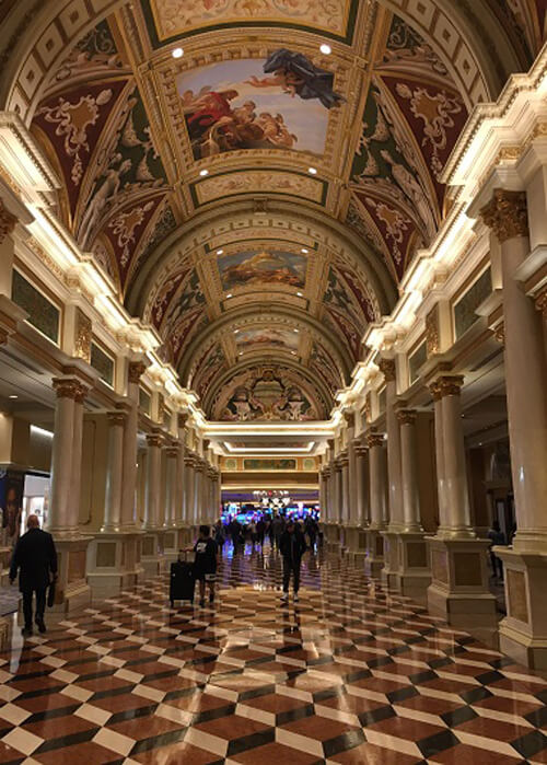 Indoor picture of Caeser's lobby in Las Vegas, with shades of brown checkerboard floors, Italian murals in the ceiling and Greek column supports. 