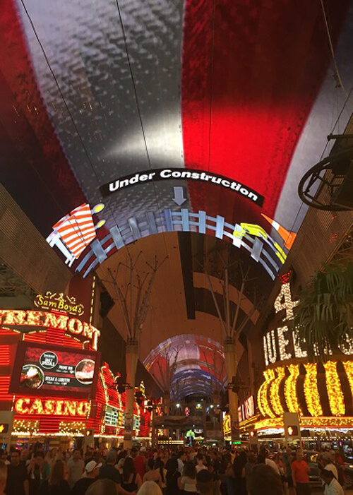 Looking down crowded Fremont Street in Las Vegas, with bright lights of yellow, red and white, and sign saying "Fremont Casino" at left and "4 Queens" at right.