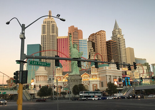 Group of buildings in downtown Las Vegas at sunrise, replica of Statue of Liberty in center. Light blue sky.