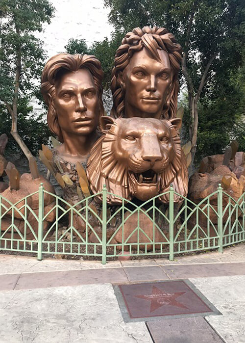 Bronze-colored statue of entertainers Siegfried and Roy with a statue of lion underneath.