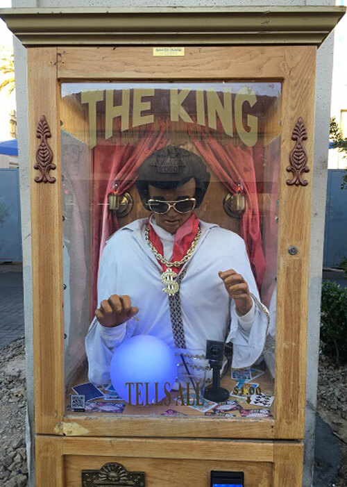 Carnival-type fortune teller machine with Elvis Presley inside wearing sunglasses and sign on glass reading "The King."