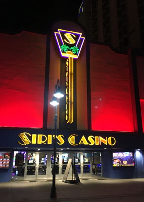 Night photo of outside of casino, with "Siri's Casino" in yellow lights and red lights descending up the building above the sign.