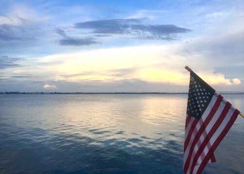 Calm ocean water reflecting the bright yellow and white clouds at sunset, with American flag at bottom right.