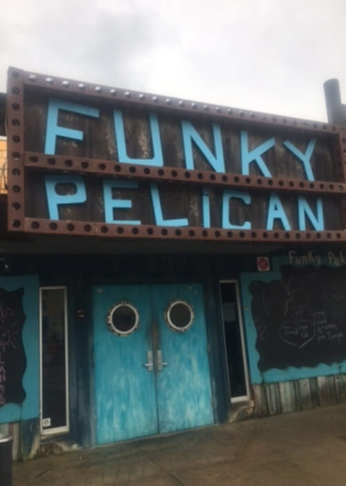 Front of Funky Pelican restaurant doors, with Funky Pelican in blue letters in sign above and two blue doors with circles for windows below.  Grey sky above.