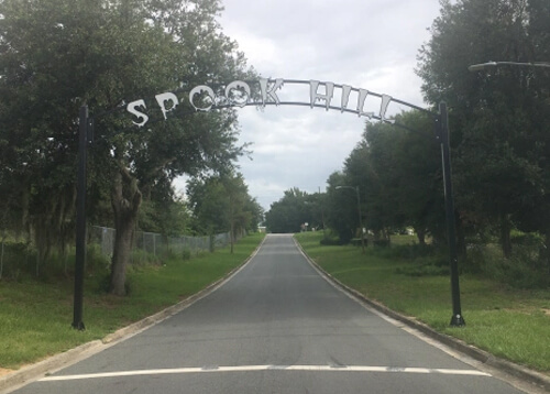 Road leading over a small hill, lined with grass and trees on both sides, and an archway above the road saying "Spook Hill."