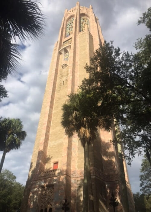 Circular light grey stone tower covers the length of the photo, with trees on both sides and cloudy grey sky above.