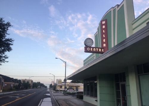 Green Art Deco style building at right saying Waller Center with a clock on it.  Street at left disappears into the horizon. Blue sky with clouds above.