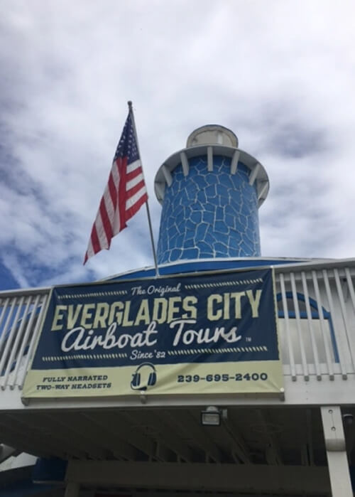 Round blue tower pointing to sky, with balcony and sign hanging from it saying "Everglades City Airboat Tours."