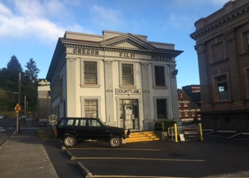 Grey early 1900's style building, two stories tall, with sign saying "Oregon Film Museum" at top.  Blue sky in background.