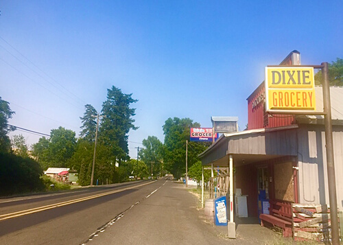 Road at left disappearing into horizon, single story market at right with yellow sign near roof reading "Dixie Grocery.