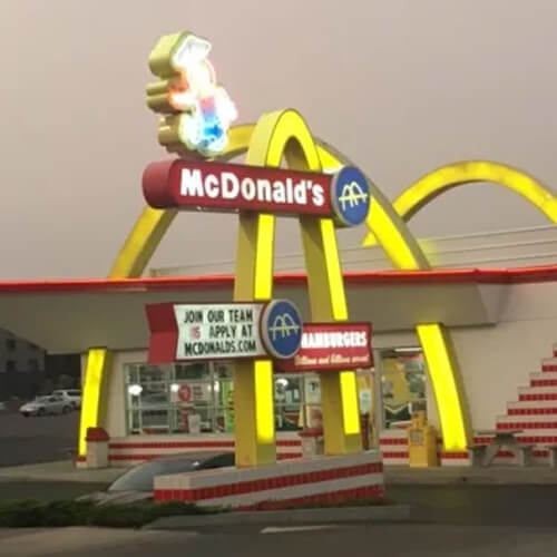 Lighted two-story-high yellow arches of McDonald's restaurant in front of white and red striped painted restaurant.  Neon character called Speedee perched on McDonald's sign.