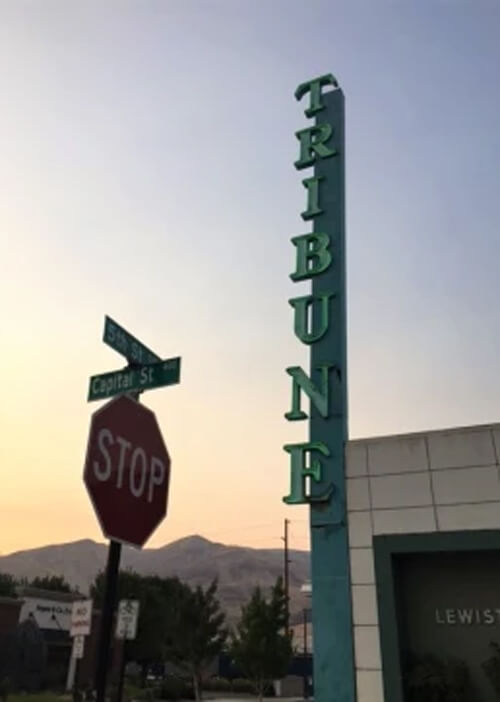 Green neon vertical sign reading "Tribune" that is about two stories tall at sundown.  Stop sign at bottom left.