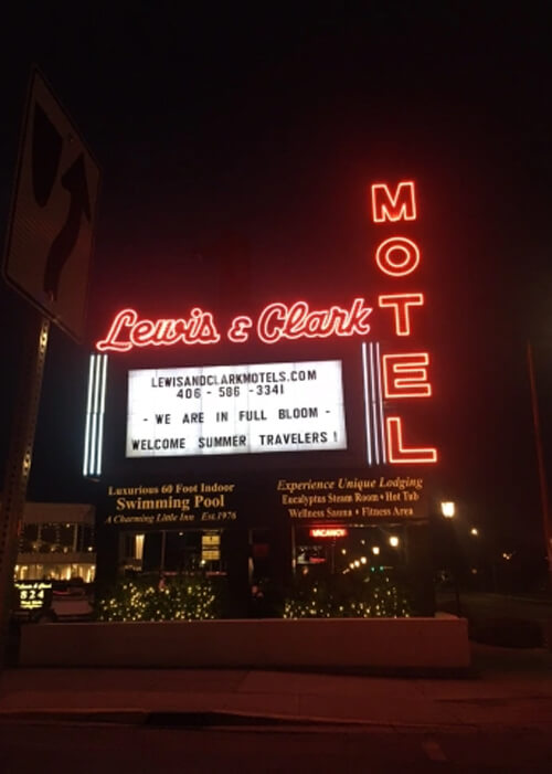 Night photo with lit red neon sign reading "Lewis and Clark Motel," with marquee below with various event announcements.