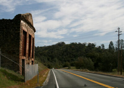 Highway aimed straight ahead into forest trees, crumbling brick building on the left, blue sky above with some clouds.