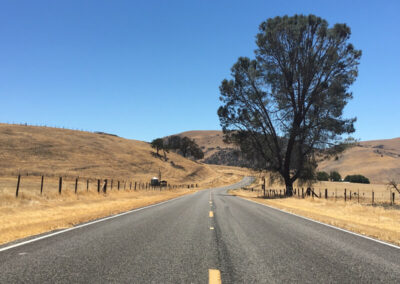 Highway aimed into range of low rolling, yellow grass covered hills, blue sky above.