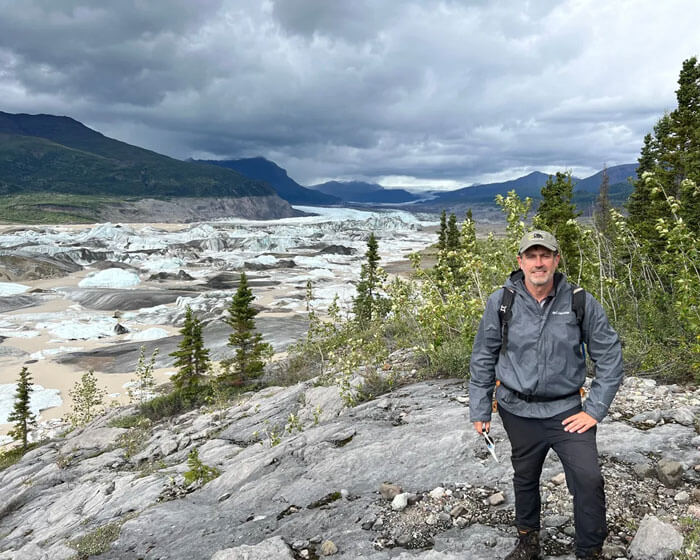 Mark Loftin posing in front of landscape scenery of mountains and green trees on a cloudy, overcast day.