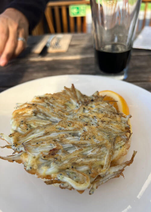 Close-up of a plate of cooked whitebait on a white plate.