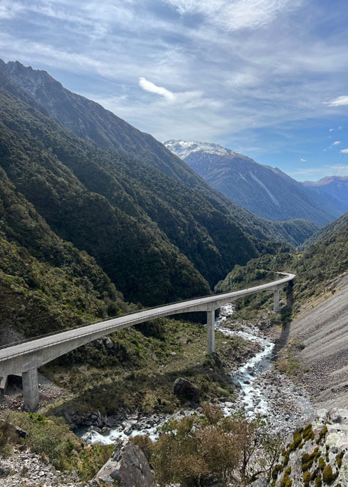 A cement viaduct elevated over a small canyon and running next to a large tree-covered mountainside.