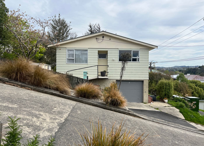 View of a house located on Baldwin Street, known as the steepest street in the world, with the angle of the street emphasized by the direction and elevation of the sidewalk in front of the house.