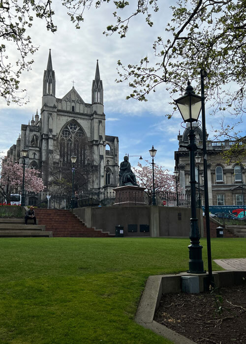 Brick steps lead up to the front of a light gray gothic church with a neatly-manicured lawn in the foreground. 