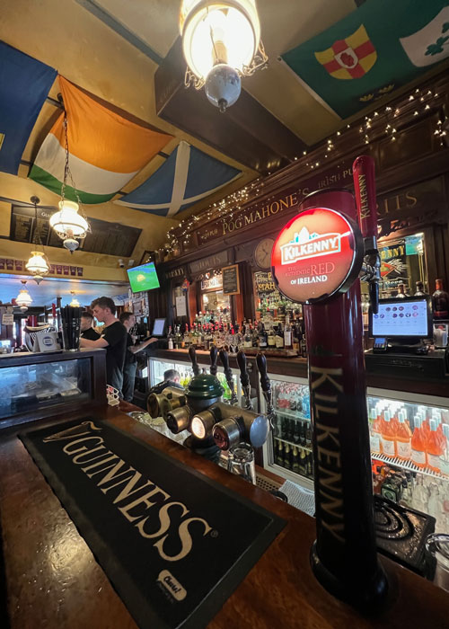 Close-up of a bar counter and bar servers behind the counter, with a Guiness sign on the bar top in a local pub.