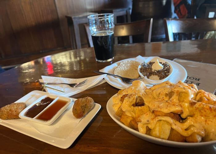 White plates of food on a table at a restaurant, featuring cheese-covered fries, haggis, and appetizers with dipping sauces.