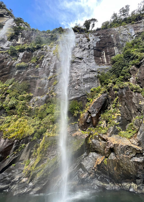 A waterfall pouring down into a body of water from a cliff covered in trees and other greenery.