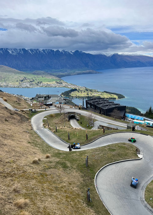 Looking down onto a concrete luge ride track with riders maneuvering down in their one-person luge vehicles.