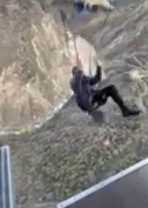 A person sitting in a harness of cables and ropes swinging and hovering across a canyon in New Zealand.